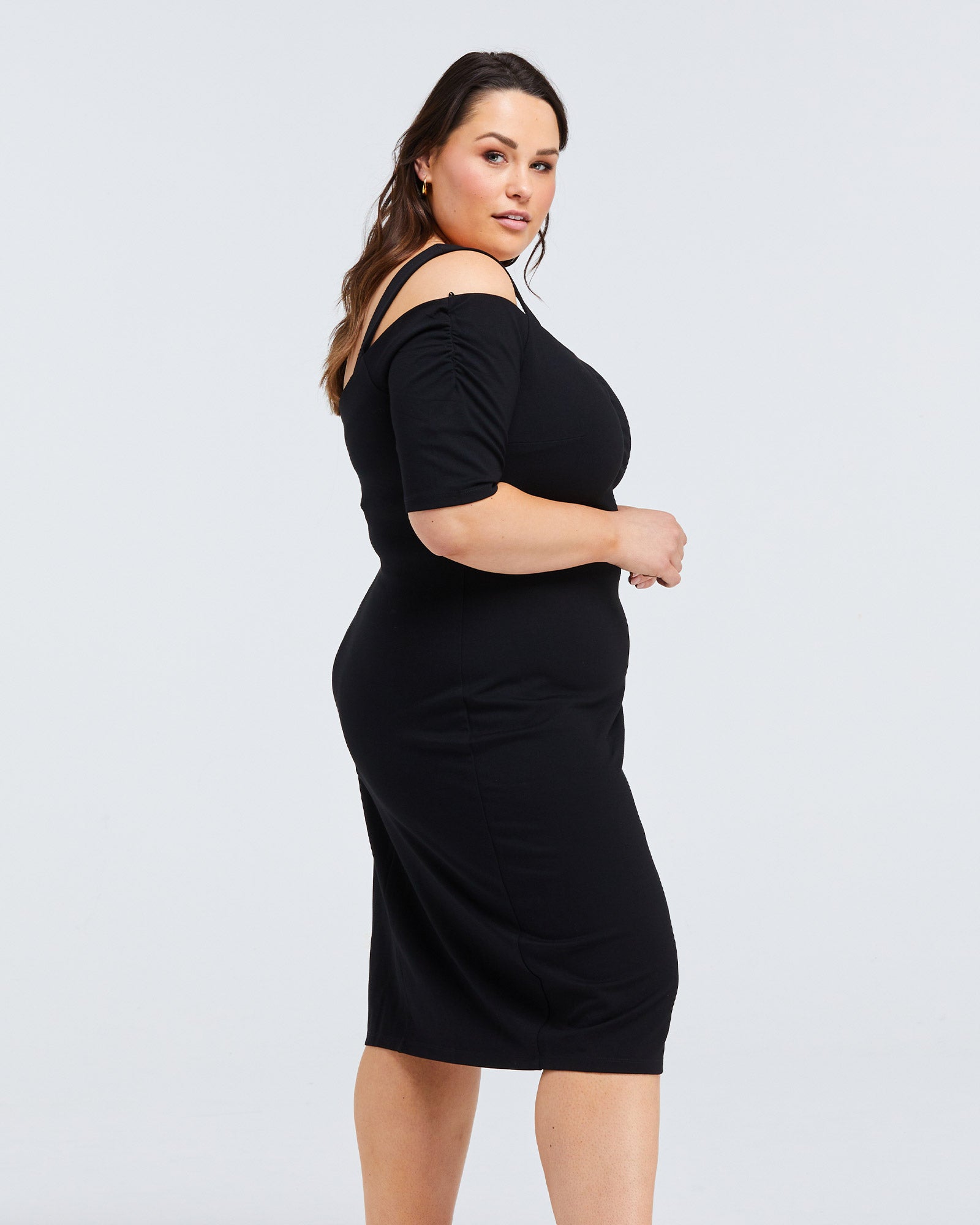 An Estelle plus size woman wearing a black cold shoulder midi Sacha Dress.