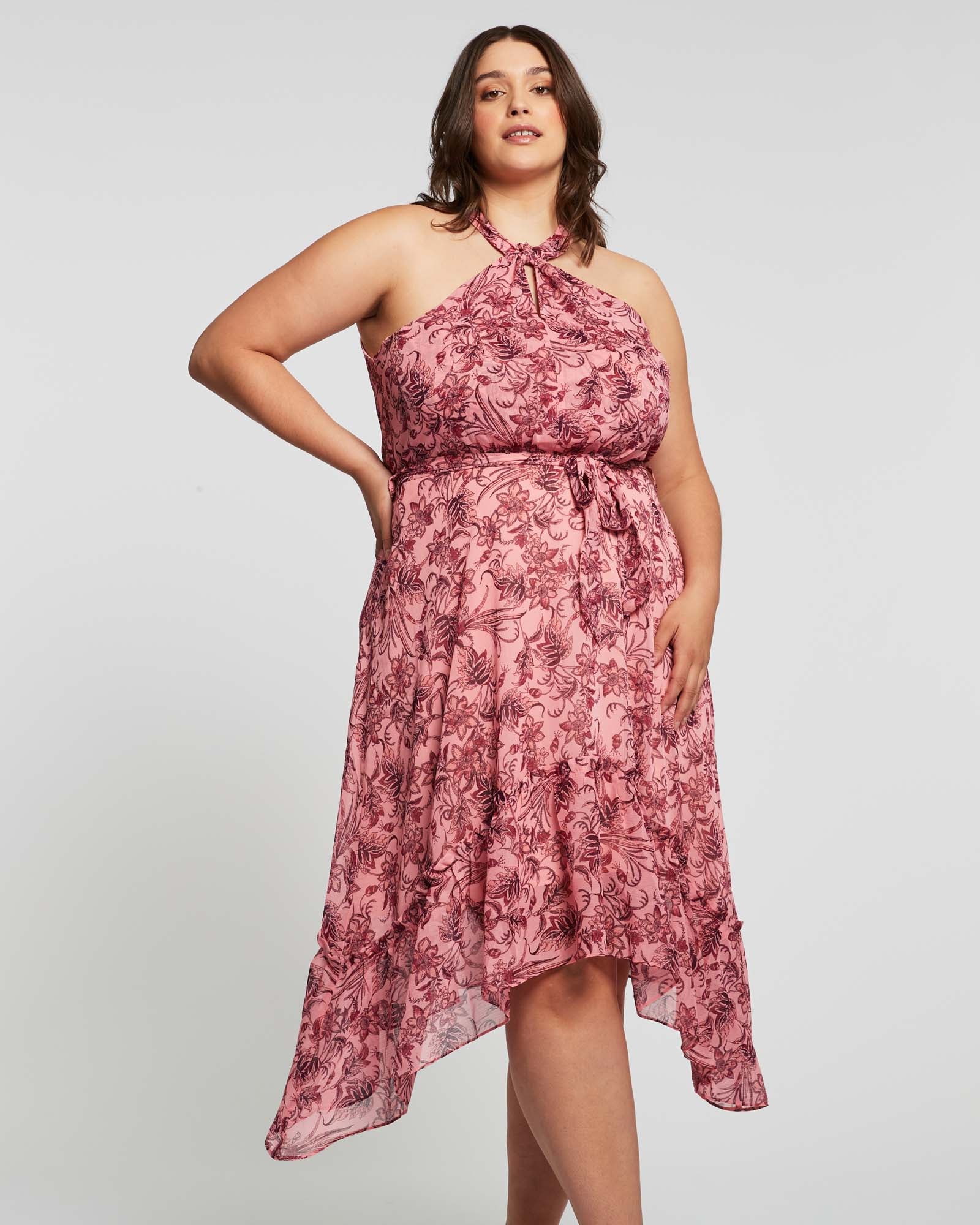 A plus size woman wearing a Estelle Sophia Halter Dress in a pink floral print.