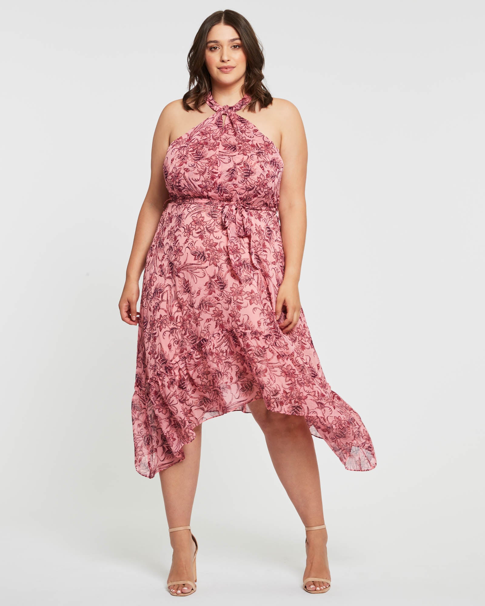 A plus size woman wearing a pink floral Estelle Sophia Halter Dress.