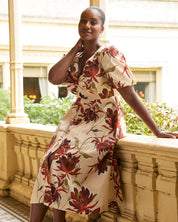 Woman in a floral dress standing on a balcony with greenery in the background