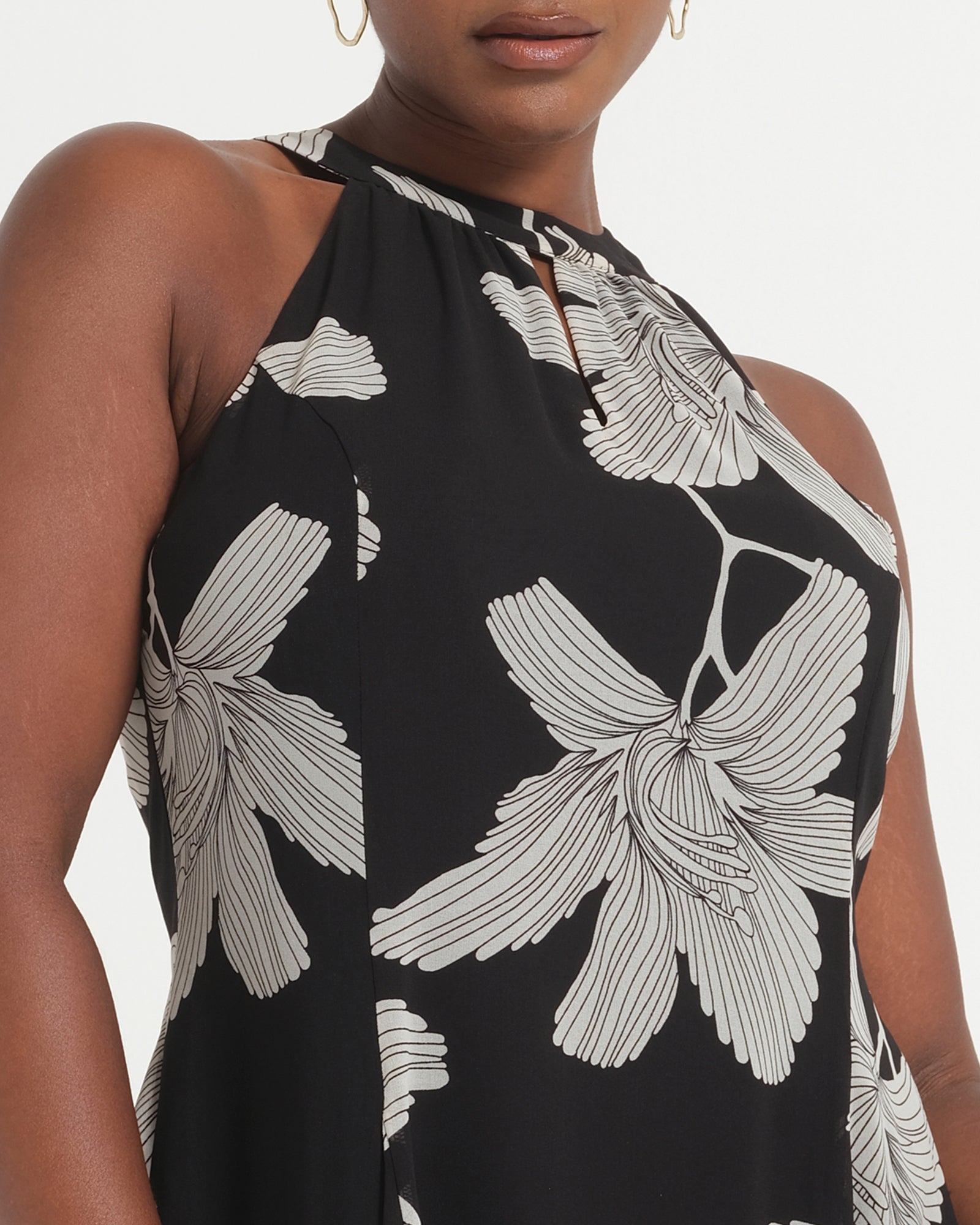 Black sleeveless top with white floral pattern worn by a model on a light gray background