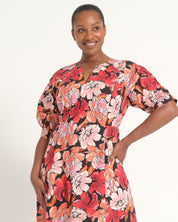 A woman modeling a short-sleeve floral dress with a keyhole neckline, standing against a plain white studio background.