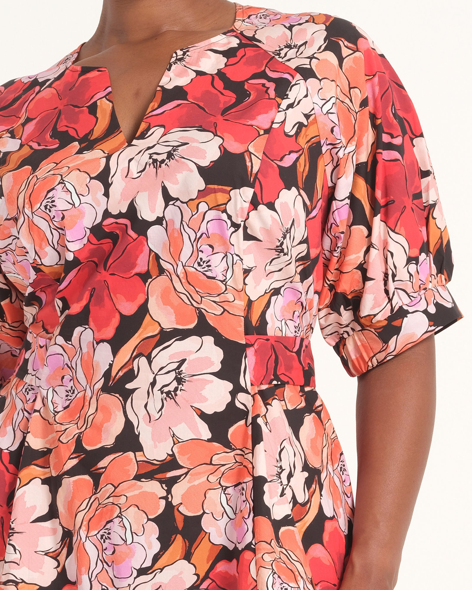 A close-up of a model wearing a short-sleeve wrap-style dress with a vibrant floral print in red, pink, orange, and white on a black background.