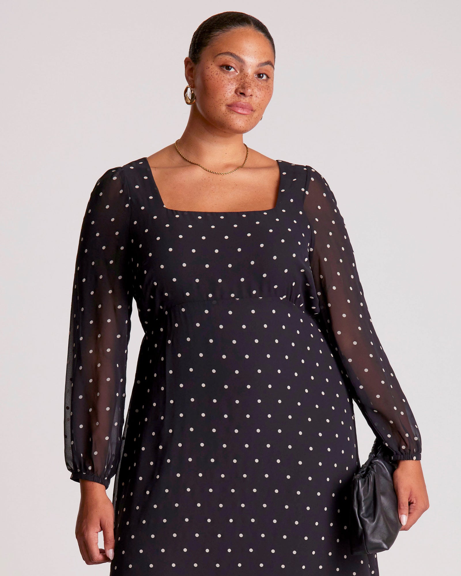 Woman wearing a black dress with white polka dots against a plain background
