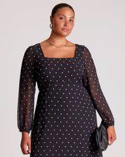 Woman wearing a black dress with white polka dots against a plain background