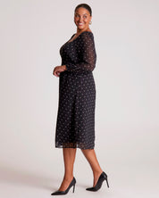Woman wearing a black dress with white polka dots on a plain background