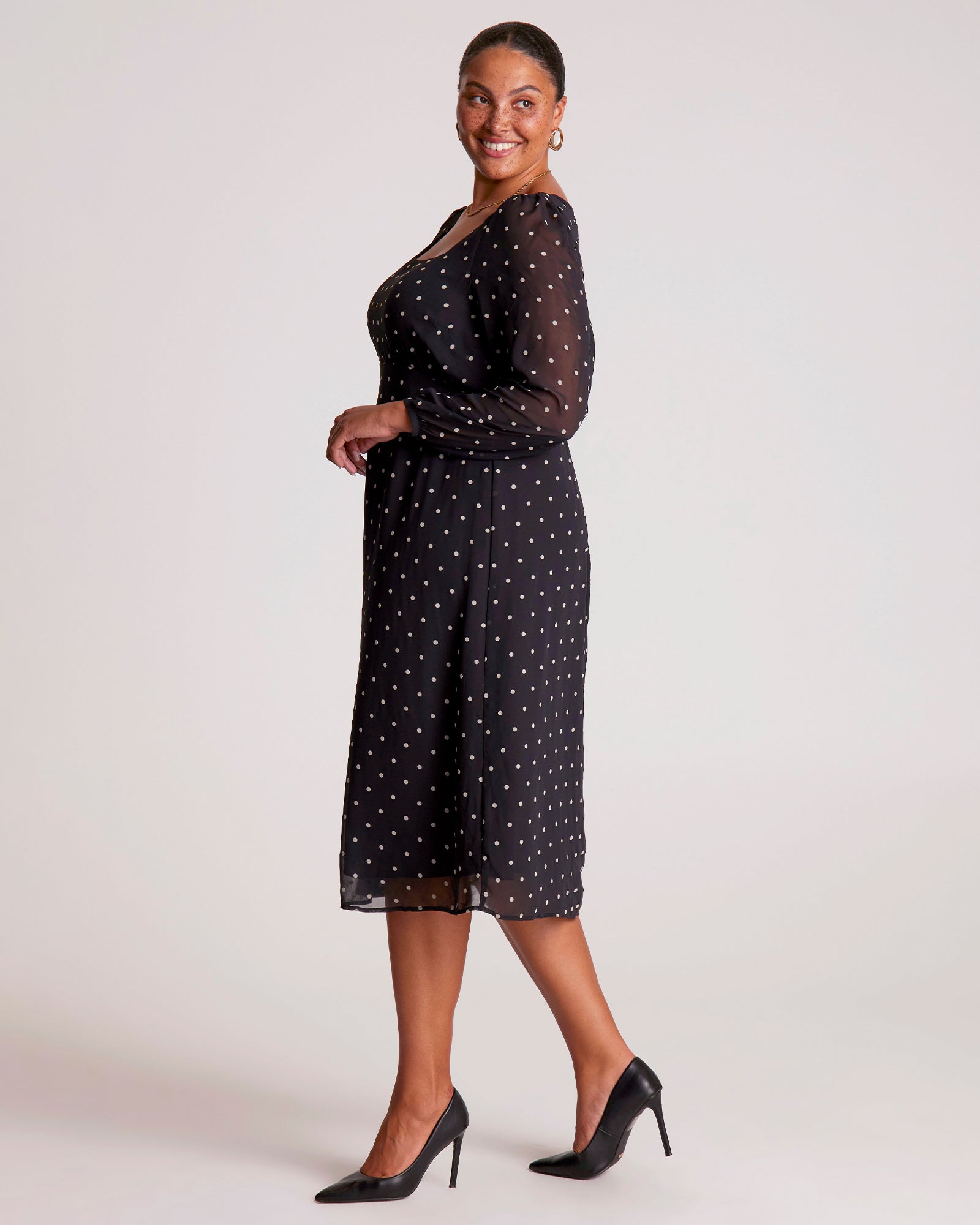 Woman wearing a black dress with white polka dots on a plain background