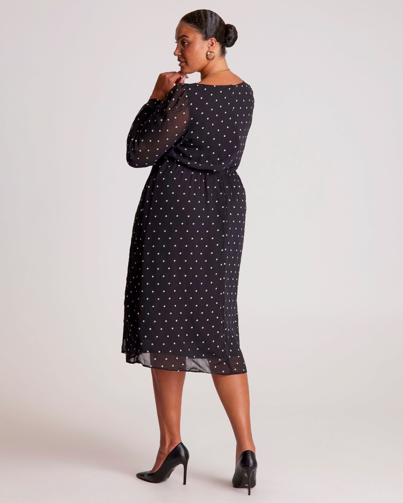 Woman wearing a black dress with white polka dots on a plain background