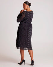 Woman wearing a black dress with white polka dots on a plain background