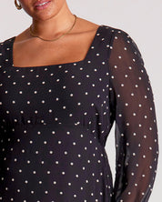 Black dress with white polka dots worn by a person on a plain background