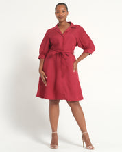 A woman modeling a red midi shirt dress with puff sleeves, a pointed collar, and a matching waist tie, photographed against a plain white studio background.