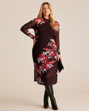 Woman wearing a dark floral dress with sheer sleeves on a beige background
