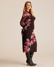 Woman wearing a dark dress with red floral pattern on a beige background