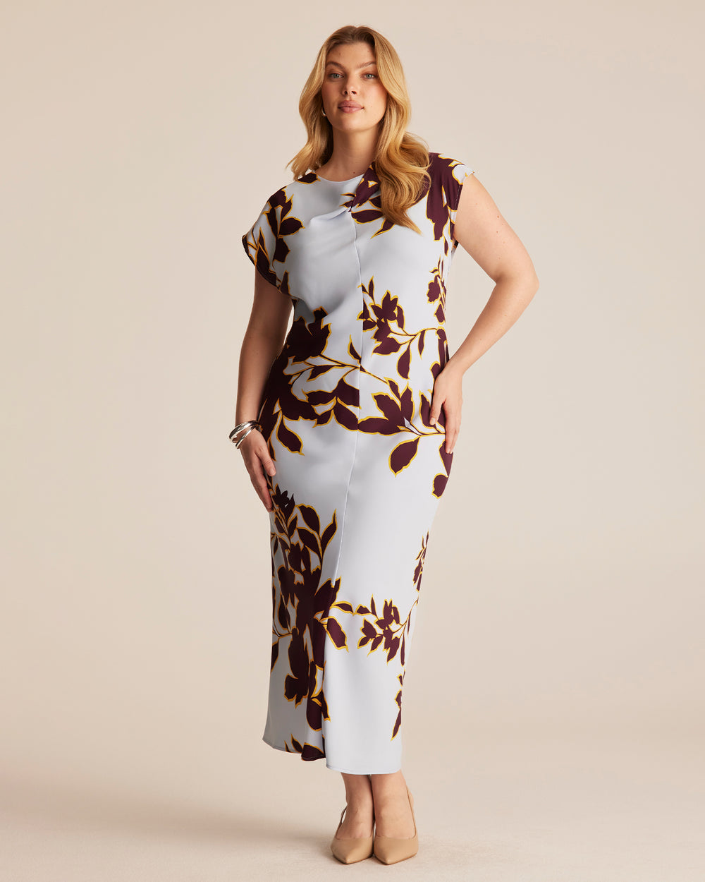 Woman wearing a blue, maroon and gold floral-patterned dress on a beige background.