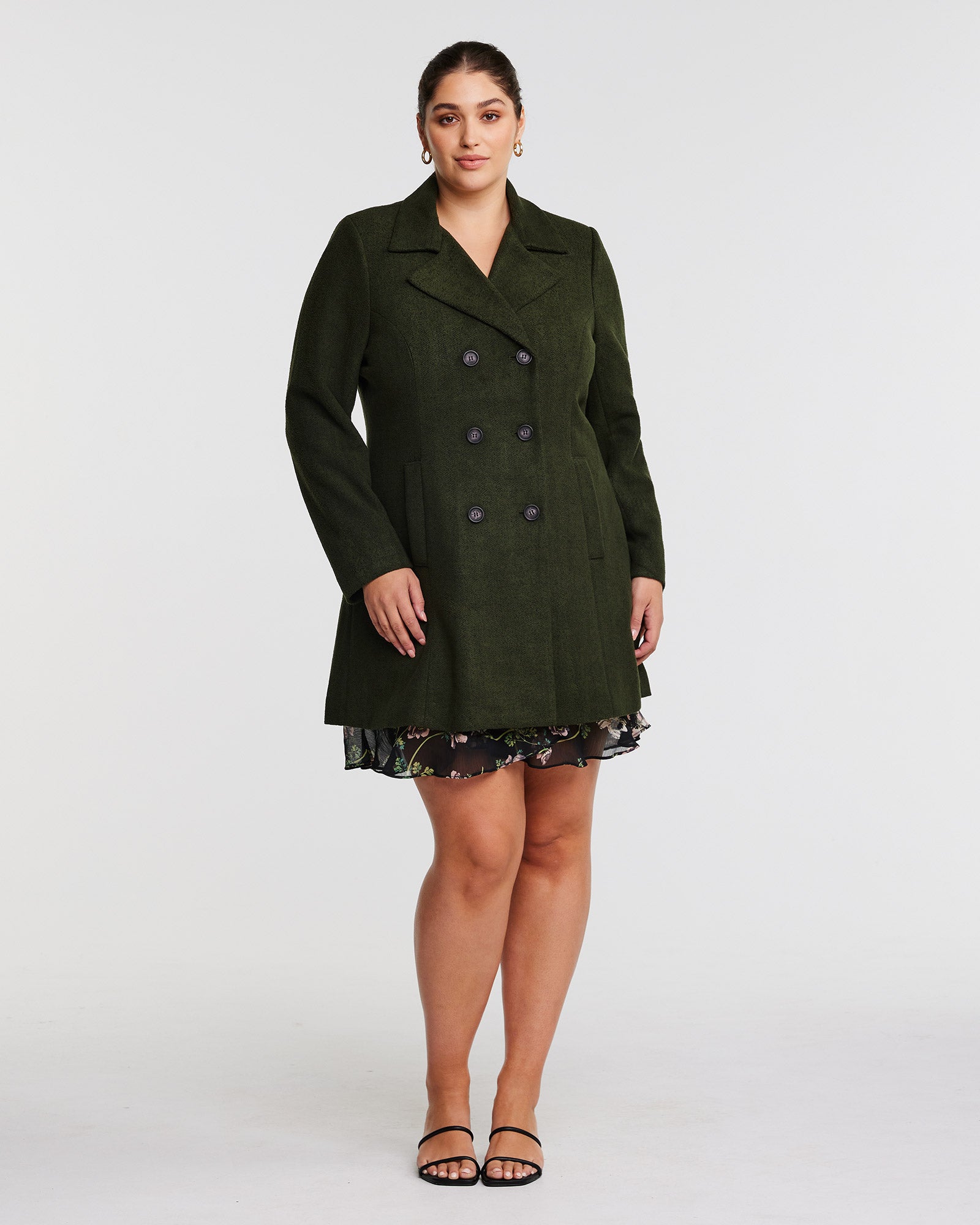 A woman wearing a olive green Homeland Coat with fully functioning pockets.