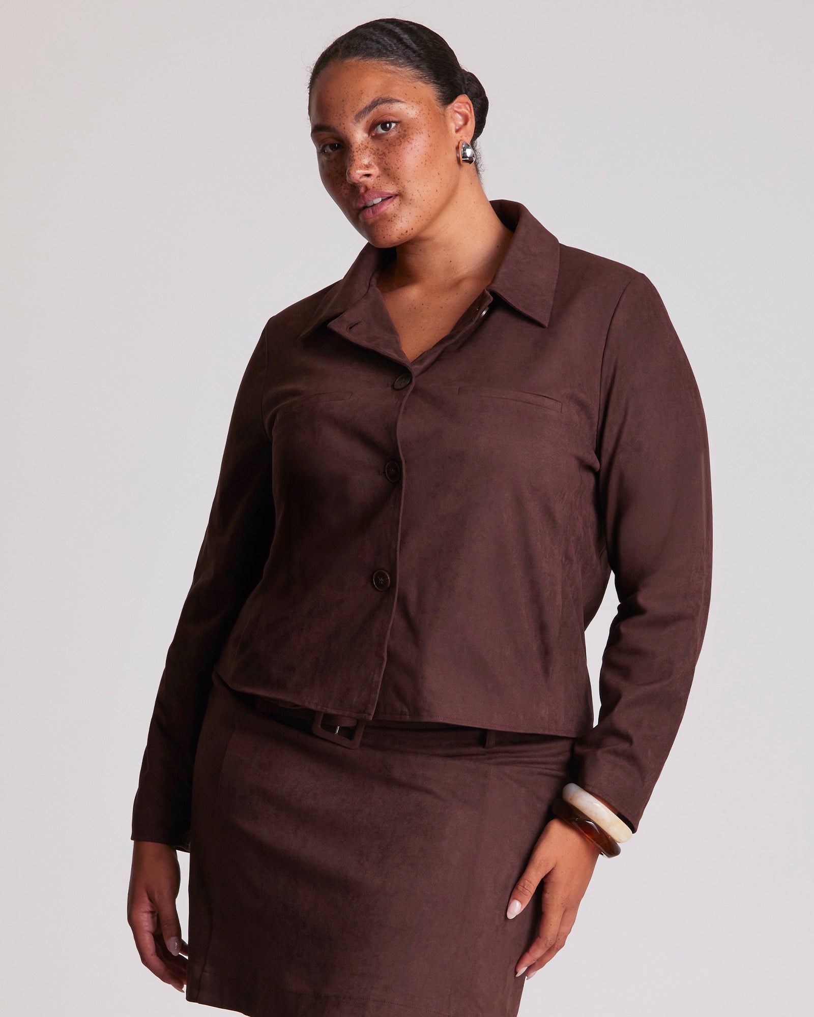 Woman wearing a brown outfit with a matching jacket and skirt on a plain background