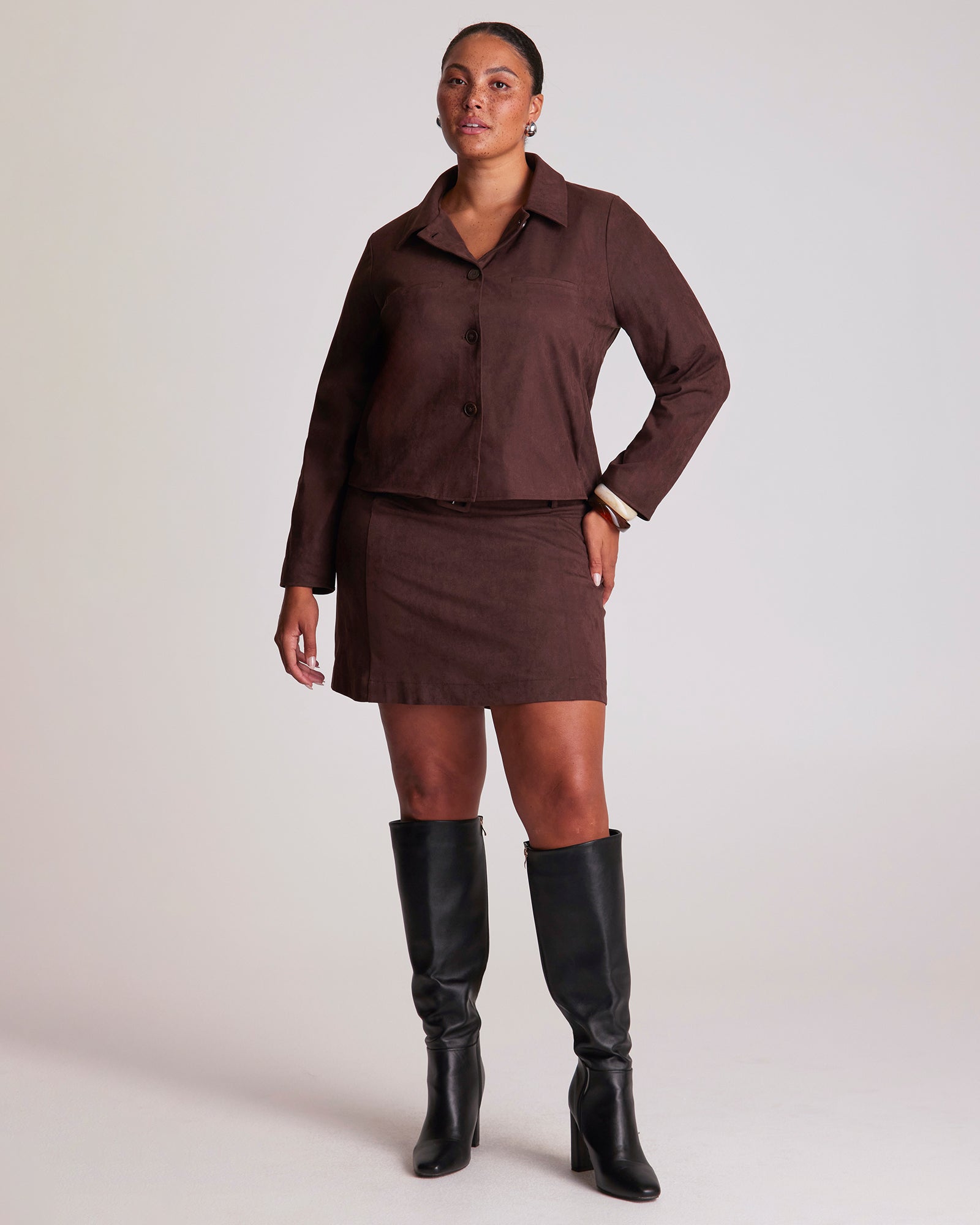 Person wearing a brown outfit with a skirt and knee-high boots on a white background