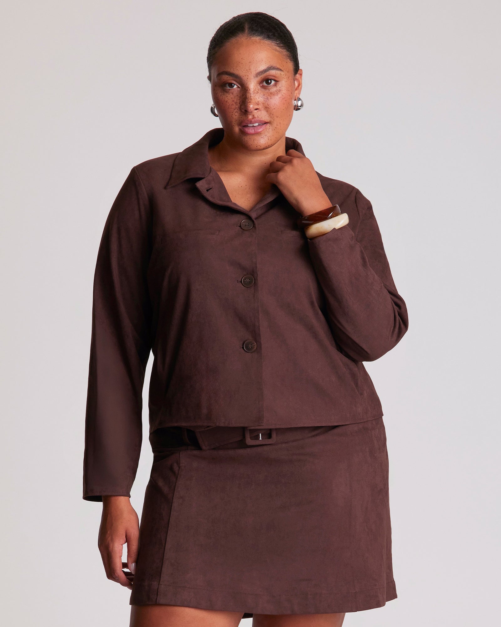 Woman wearing a brown outfit with a jacket and skirt on a plain background