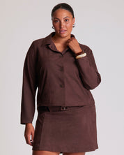 Woman wearing a brown outfit with a jacket and skirt on a plain background