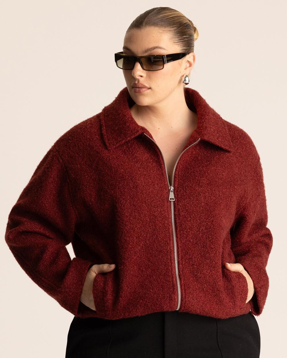 Woman wearing a deep red collared jacket with a silver chrome handbag against a neutral background