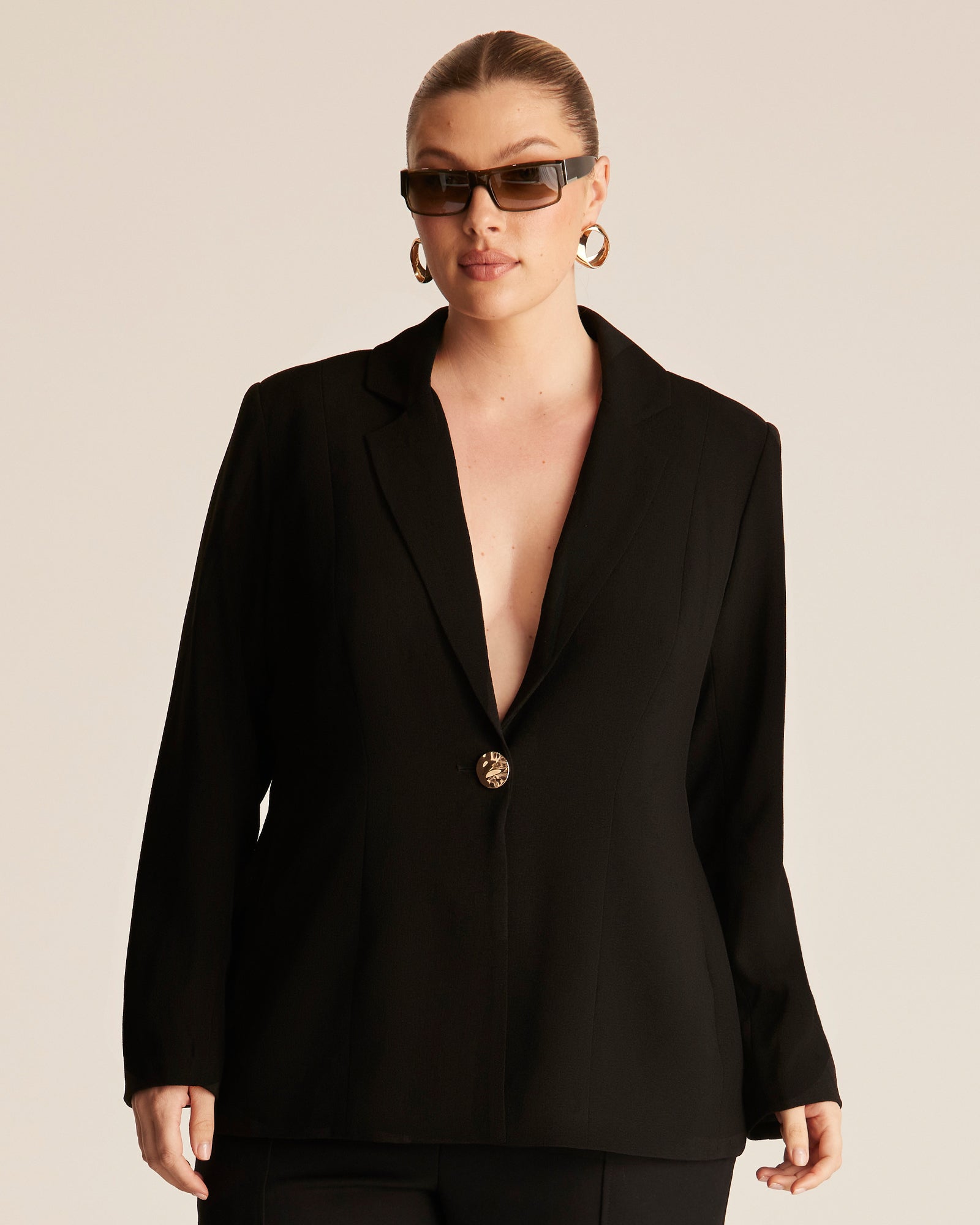 Person wearing a black blazer with a deep neckline on a beige background