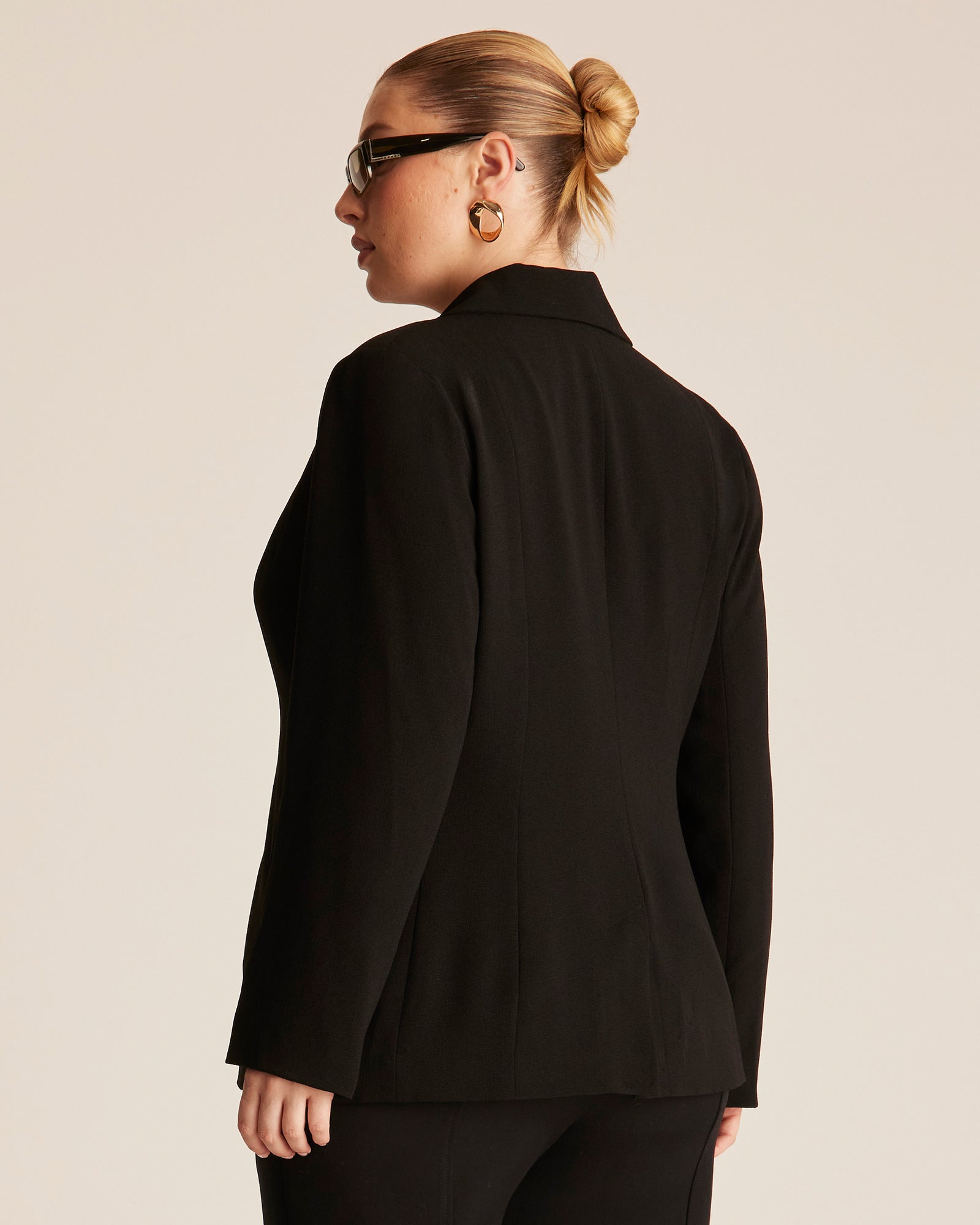 Person wearing a black blazer from behind on a beige background