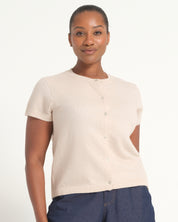A woman wearing a short-sleeve cream-colored knit cardigan with a button-up front, paired with dark blue jeans, against a plain white studio background.
