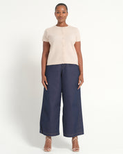 A woman modeling a cream short-sleeve button-front top paired with navy wide-leg cropped pants and nude strappy heels, photographed against a clean off-white studio background.
