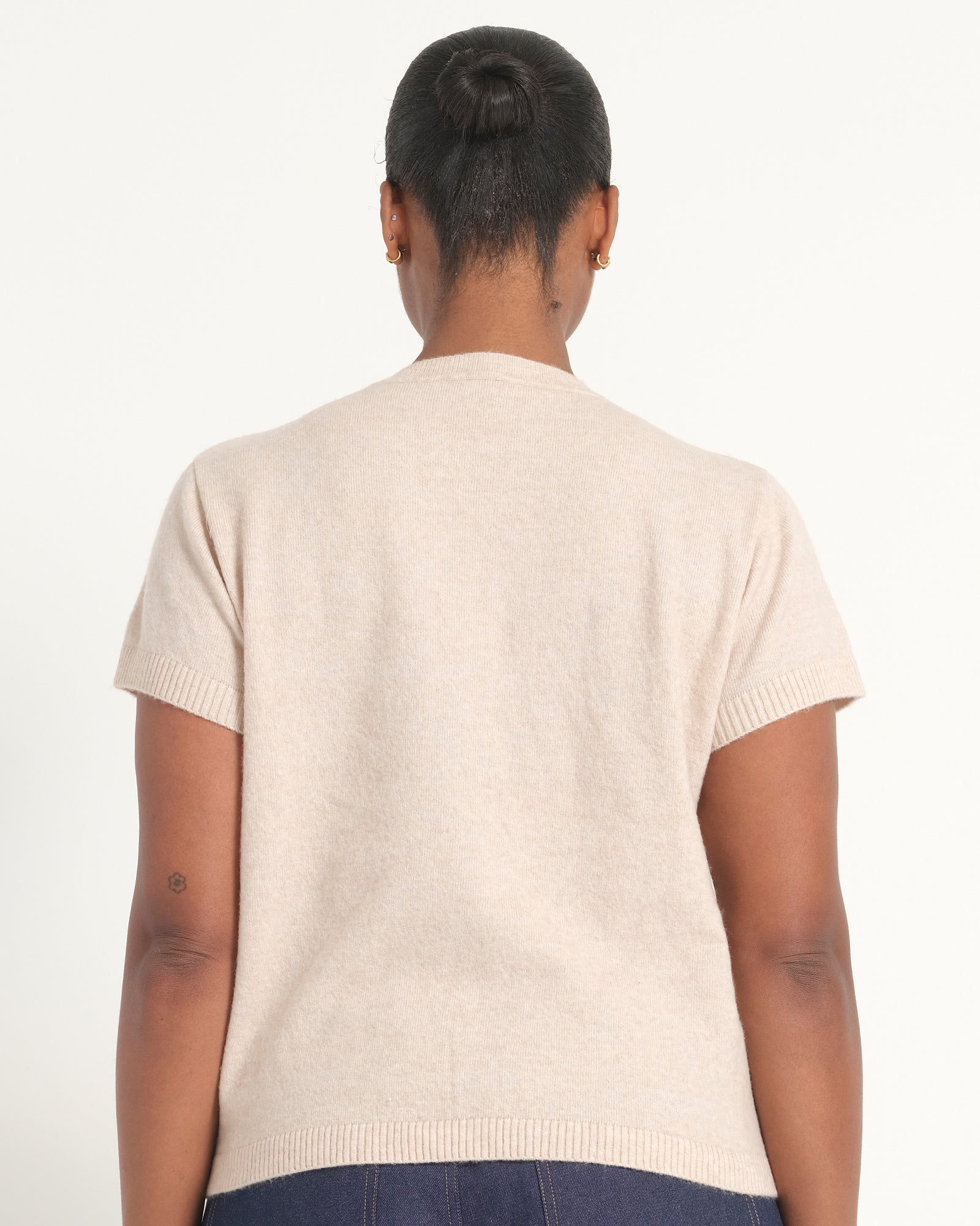 A person shown from the back wearing a short-sleeve knit top in a light cream or oatmeal color, photographed against a plain light background.