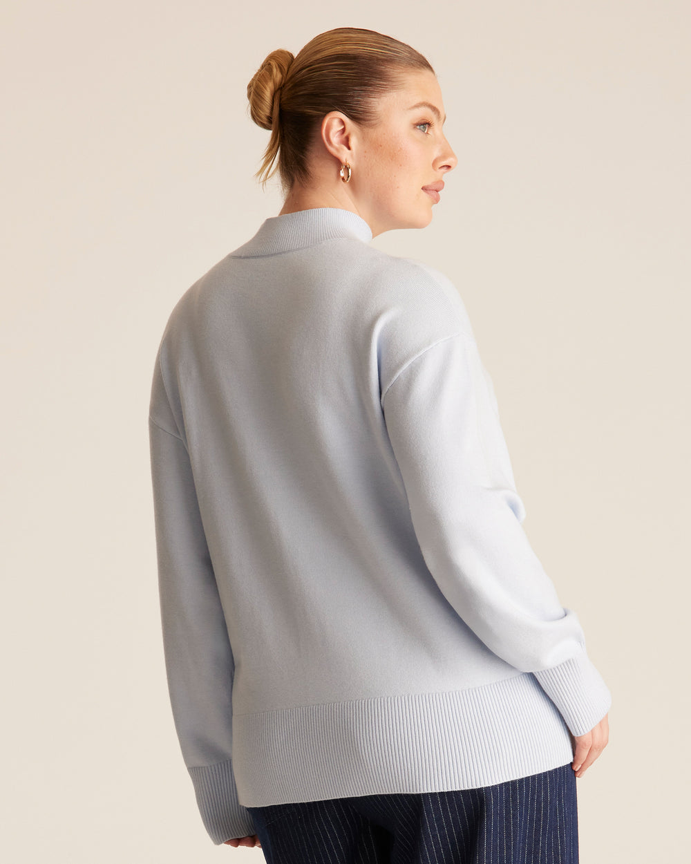 Woman wearing a light blue high neck knit sweater against a beige background.