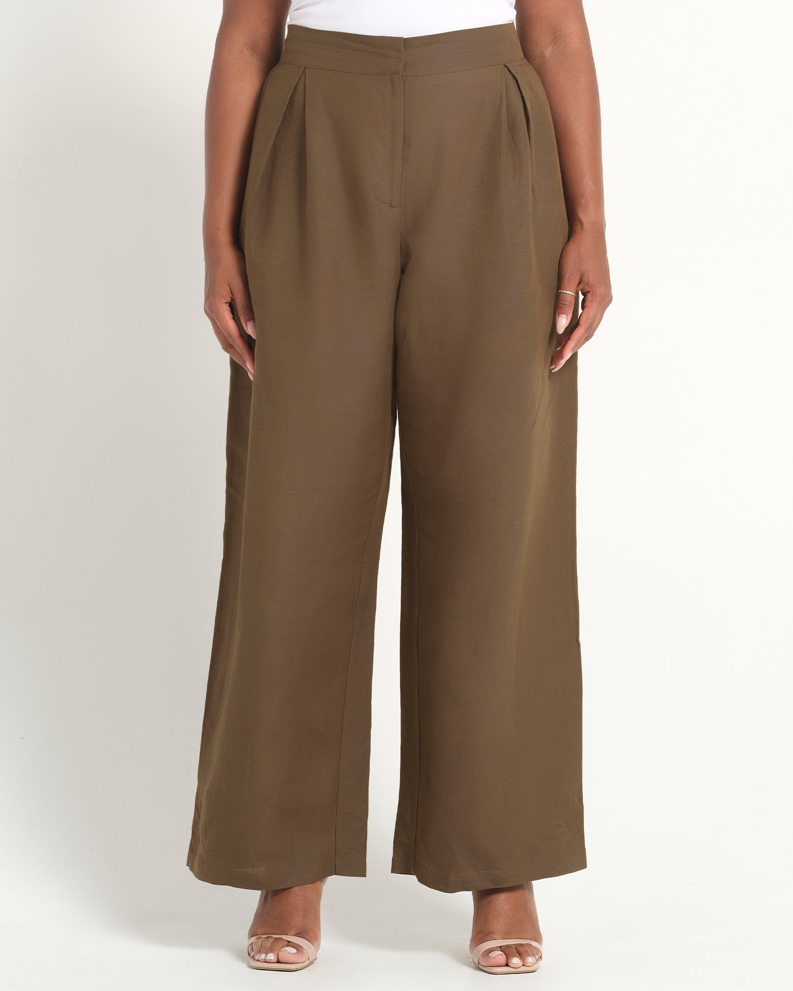 A model wearing a pair of wide-leg cropped pants in a solid taupe-brown color, paired with a white top and clear high-heeled sandals, photographed against a clean white studio background.