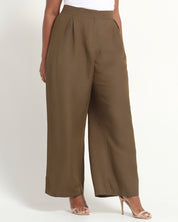A model wearing high-waisted, wide-leg trousers in a solid taupe-brown color, styled with a white top and clear high-heeled sandals against a plain white studio background.