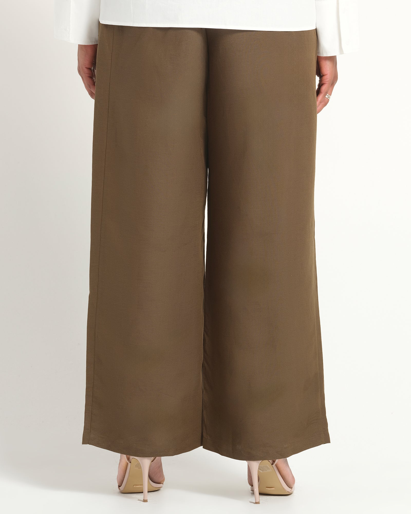 A person shown from the back wearing wide-leg cropped pants in a warm taupe-brown color, paired with a white top and beige heels, against a plain light background.