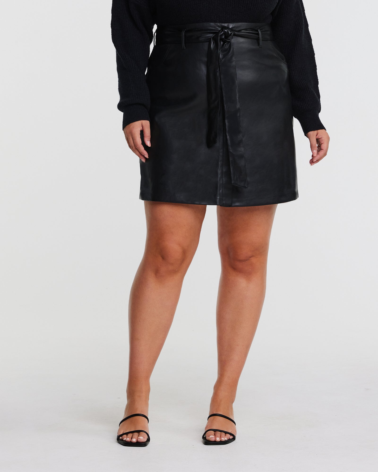 A plus-size fashionista wearing a Black PU Vegan Leather Belted Skirt.