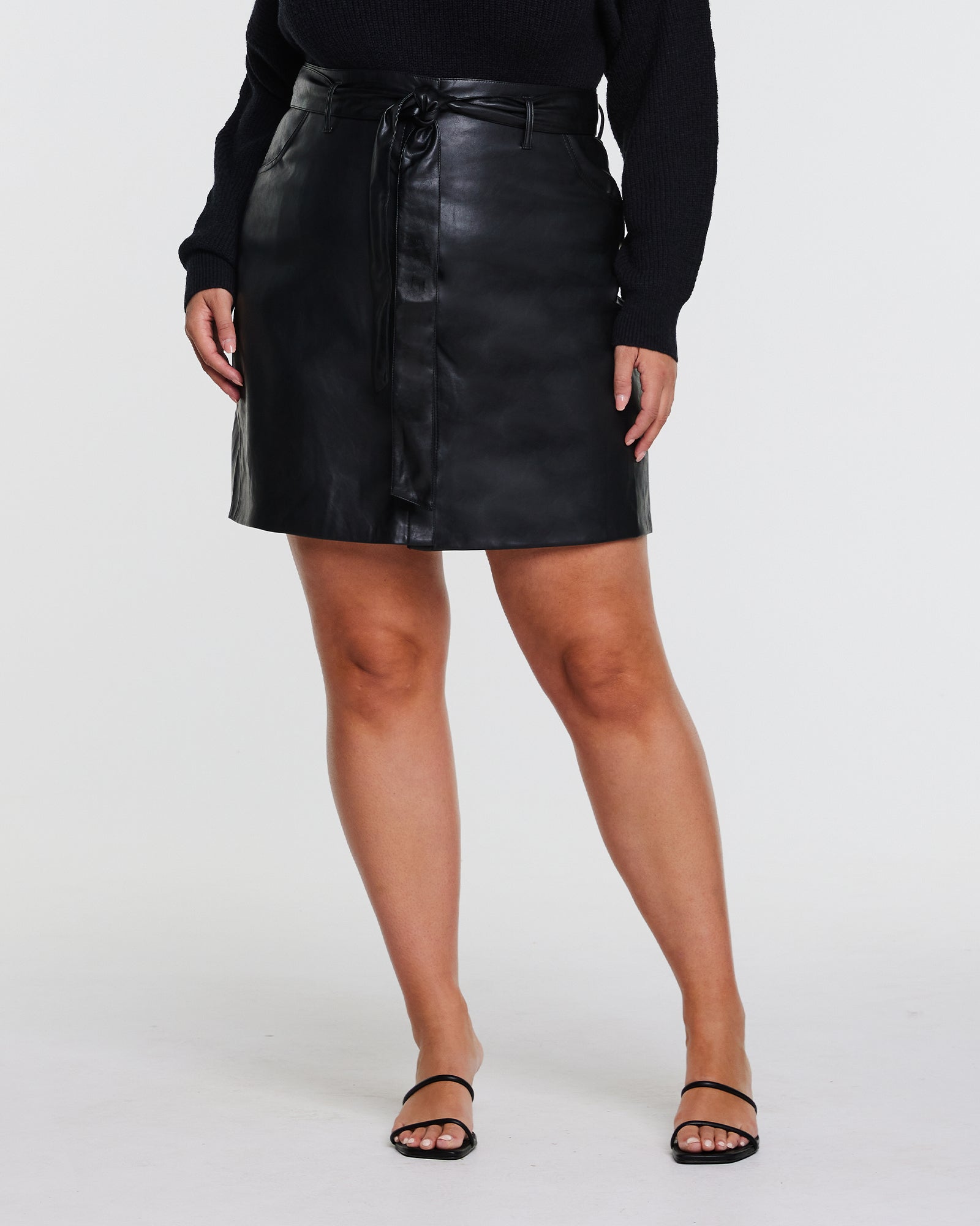 A plus-size fashionista wearing a Black PU Vegan Leather Belted Skirt.