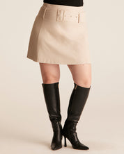 Person wearing a beige skirt and black knee-high boots on a beige background