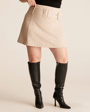 Person wearing a beige skirt and black knee-high boots on a plain background
