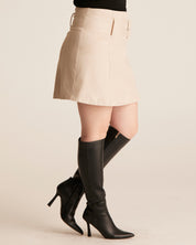 Person wearing a beige skirt and black knee-high boots on a beige background