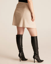 Person wearing a beige skirt and black knee-high boots on a beige background