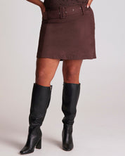 Person wearing a brown skirt and black knee-high boots on a plain background