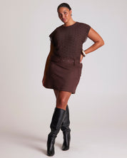 Woman wearing a brown dress with a belt and black knee-high boots on a white background