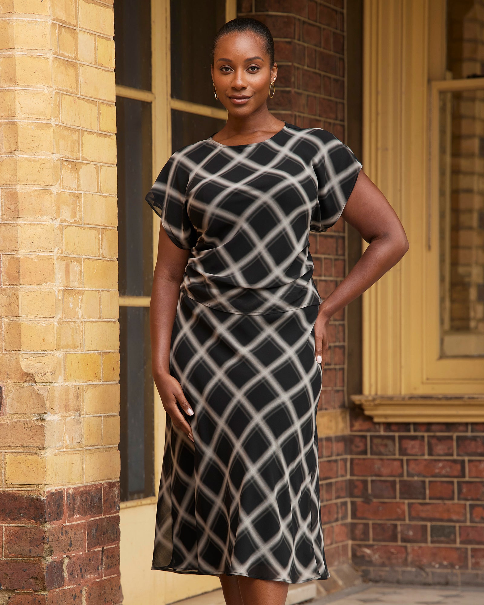 Woman wearing a black and white patterned dress standing in front of a brick building.