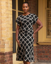 Woman wearing a black and white patterned dress standing in front of a brick building.