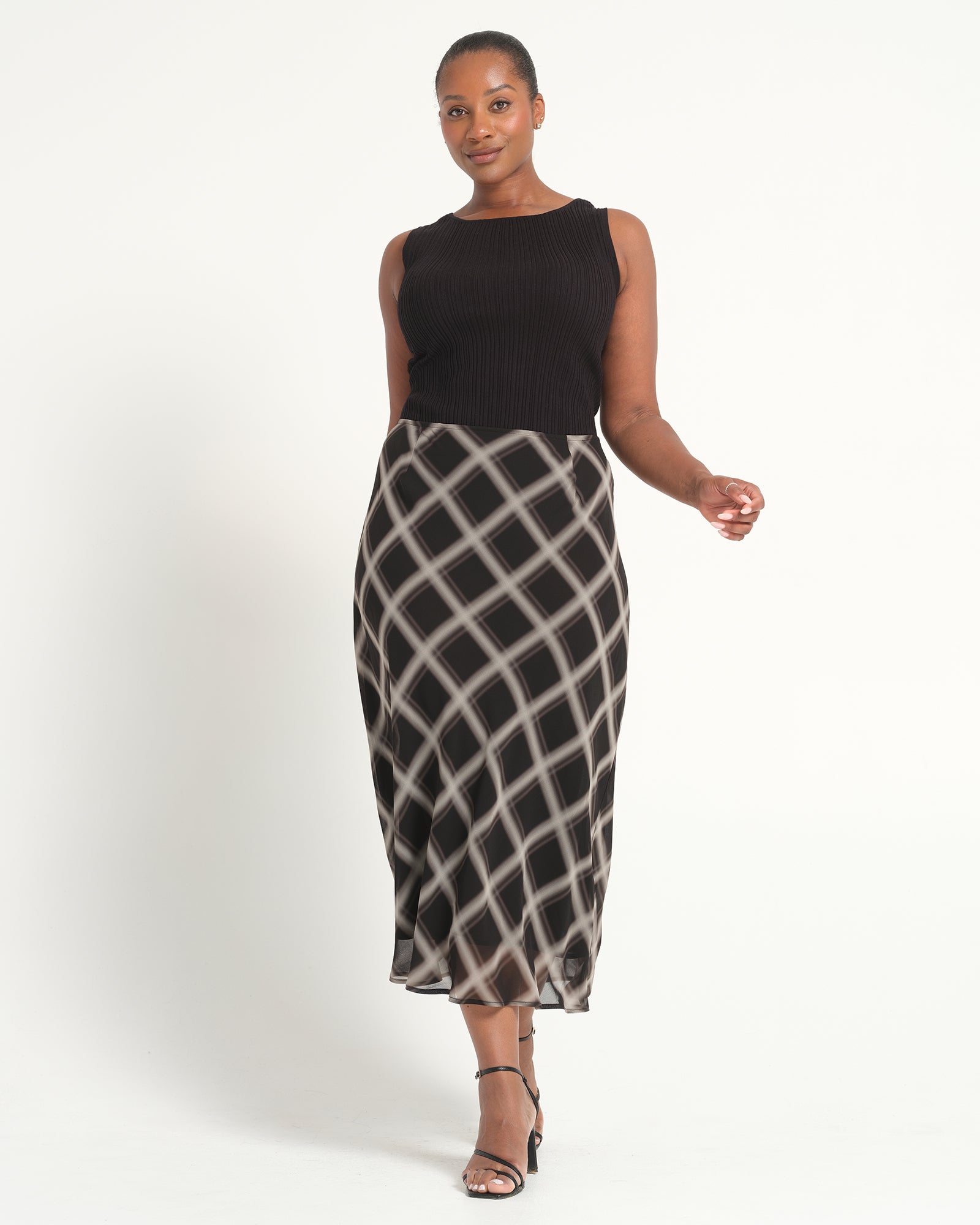 Woman wearing a black sleeveless top and patterned skirt on a white background