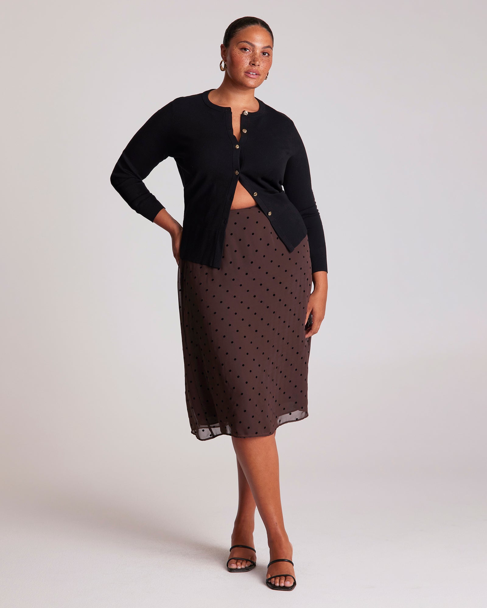 Woman wearing a black cardigan and patterned skirt on a white background