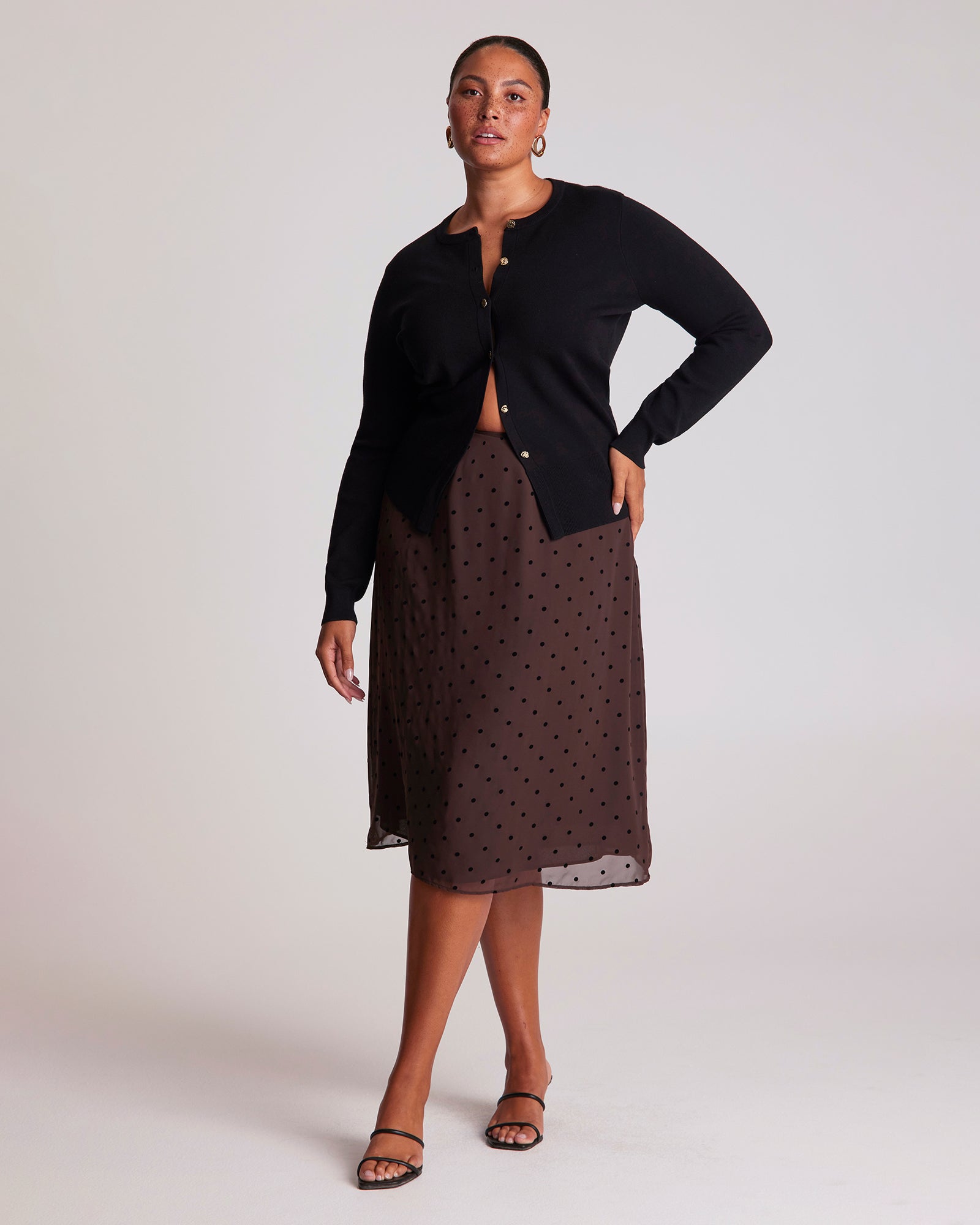 Woman wearing a black cardigan and brown polka dot skirt on a white background