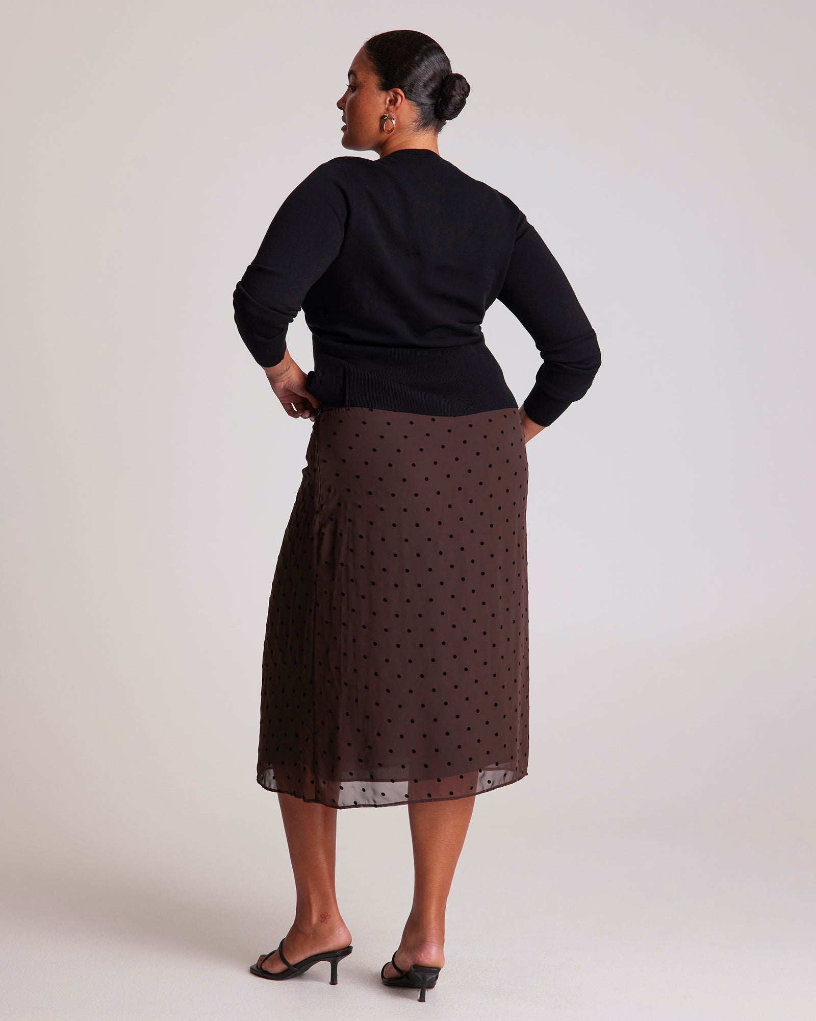 Person wearing a black top and brown polka dot skirt on a white background