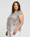 A plus size woman wearing an Estelle Nautilus Top and white pants.