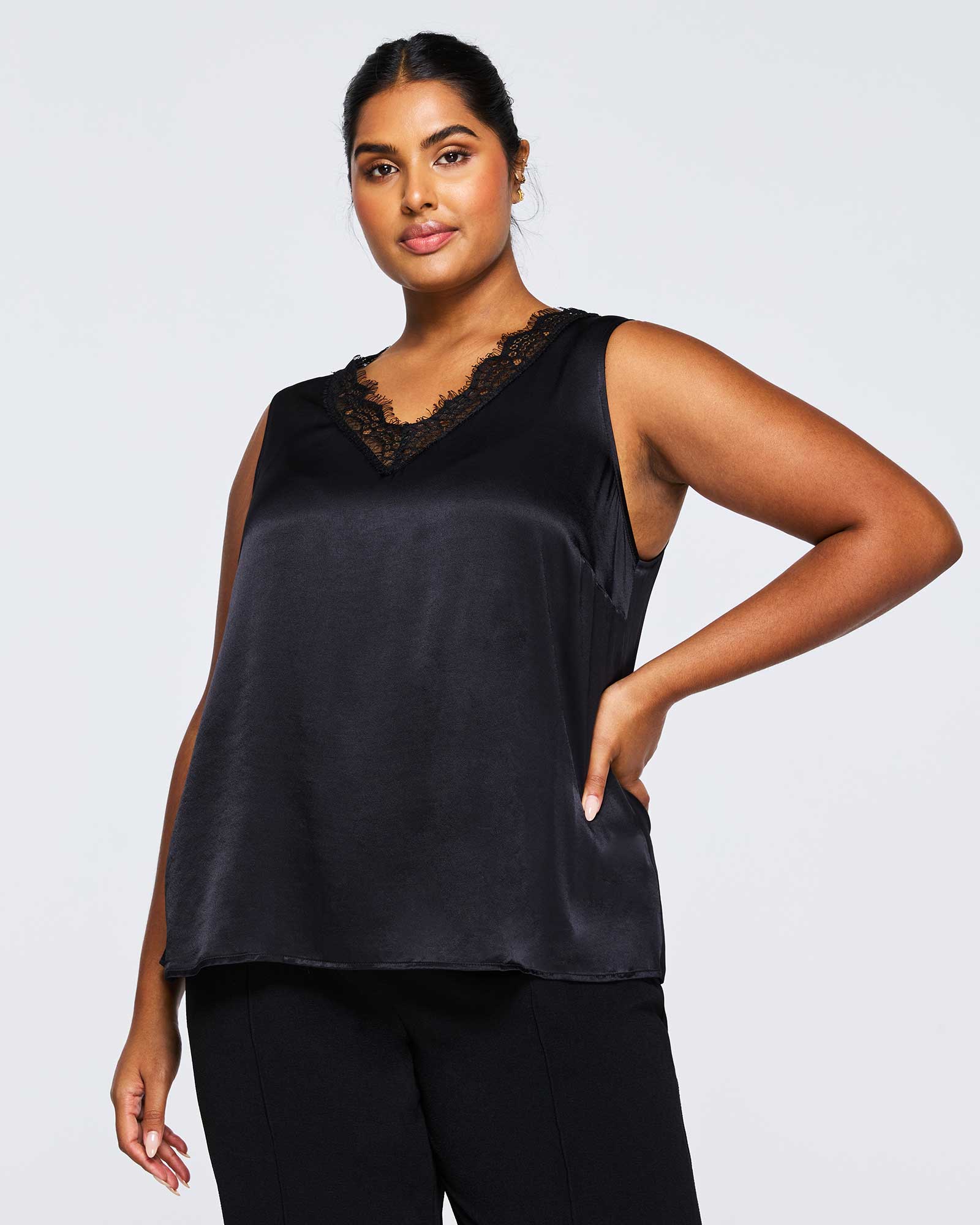 A plus size woman wearing an Alessandra Black Lace Satin Camisole Top by Estelle-us and black pants.