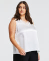 A plus size woman wearing an Estelle white silk Alessandra Cami top and black pants.